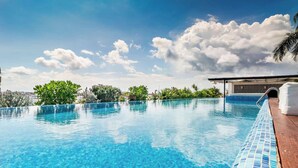 A clear blue swimming pool with a tiled edge, surrounded by greenery and a clear sky. - 2BR condo w/ pools, gym & balcony, steps to beach (Playa del Carmen)