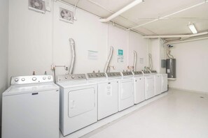 Uma lavanderia equipada com várias máquinas de lavar e secar, dutos de ventilação e um aquecedor de água.