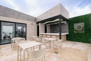 An outdoor seating area with tables and chairs, a bar, and a green hedge wall. - Rooftop pool studio | steps to Coco Beach (Playa del Carmen)