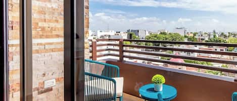 A balcony with a view of a cityscape, a small table with a plant, and two chairs.