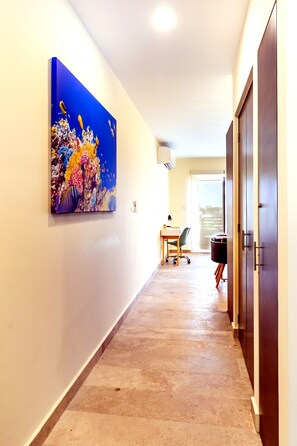En hall med ett klinkergolv, ett skrivbord med en stol, en dörr och en väggmonterad luftkonditioneringsenhet.