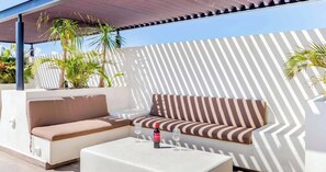An outdoor seating area with a sofa and a table, a bottle of wine, and potted plants. - Veranto condo near 5th Ave w/ pool access (Playa del Carmen)