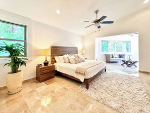 A bedroom with a bed, nightstands, a ceiling fan, a large window, and a view of the outdoors.