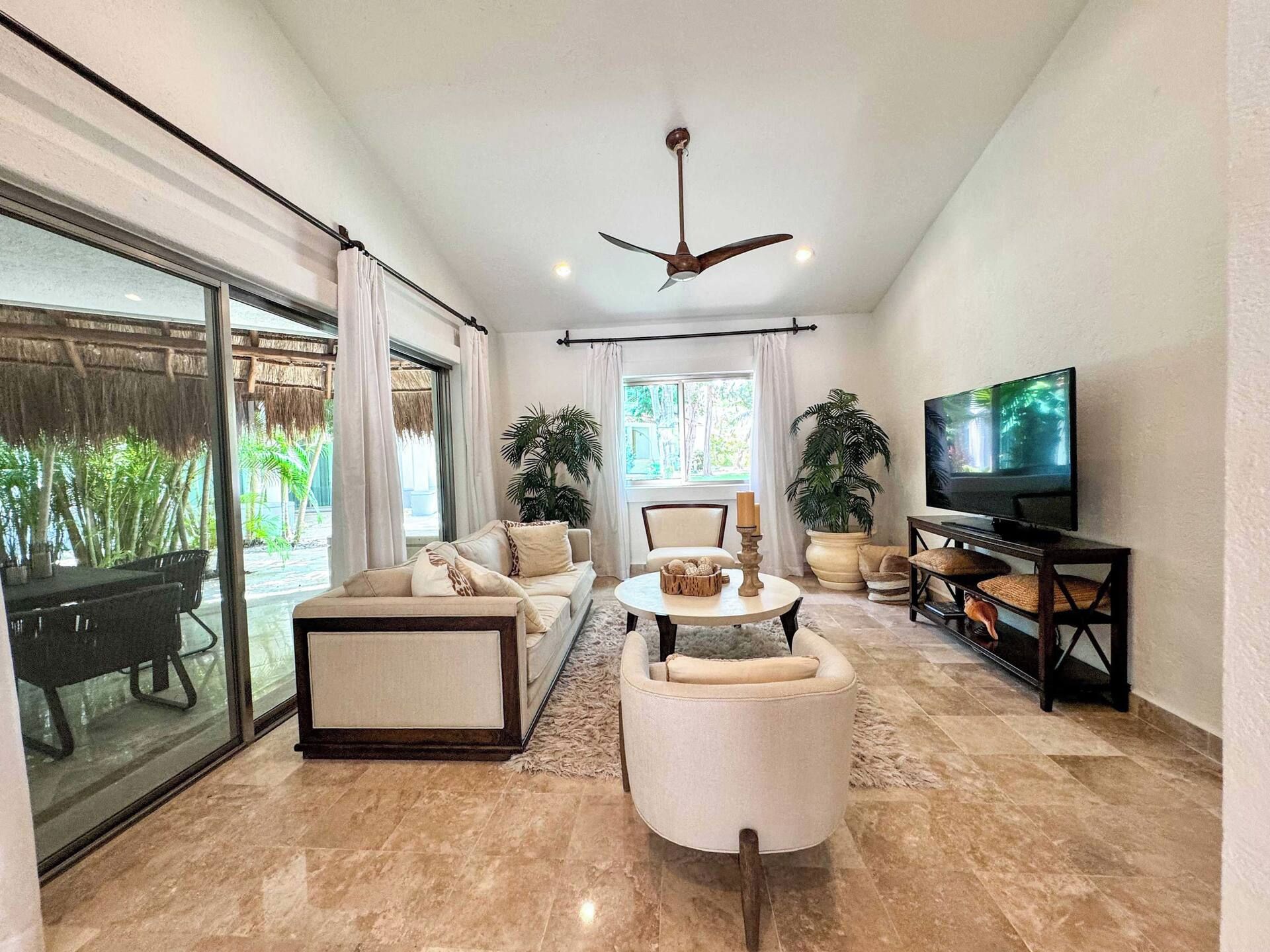 A spacious living room with a large TV, comfortable seating, and a view of greenery outside.