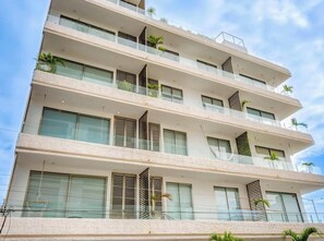 A multi-story building with balconies, large windows, and some greenery. - Serene Ocean Views, Infinity Pool, Gym and Balcony (Playa del Carmen)