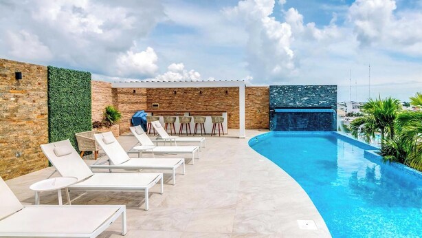Zona de piscina con sillones de descanso, bar y pared de piedra.