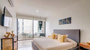 Un dormitorio moderno con una cama grande, un televisor y un balcón con sillas.