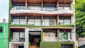 Un edificio de varios pisos con jardín en la azotea, ventanas grandes y una entrada visible.