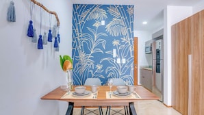 Un comedor con pared azul estampada, una mesa de madera y una cocina visible al fondo.