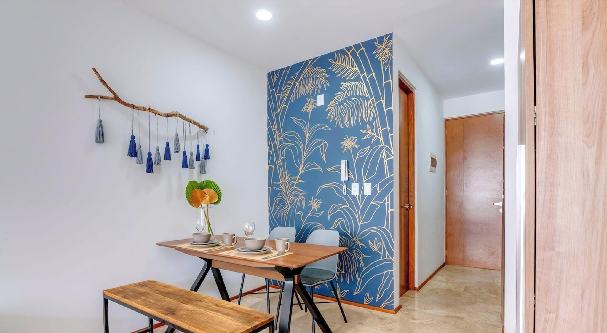 Un comedor con una mesa, sillas, un banco, un muro decorativo y una puerta.