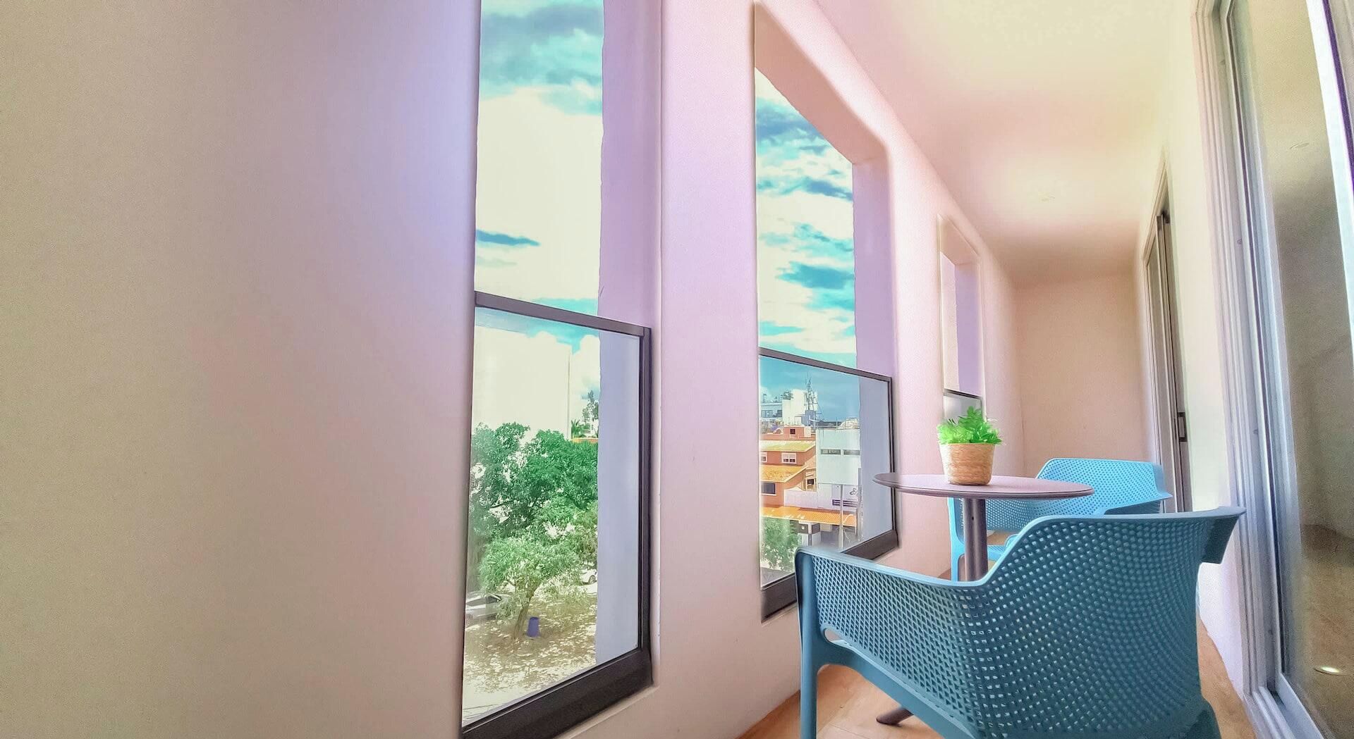 Een balkon met uitzicht op gebouwen en bomen, een kleine tafel met een plant en blauwe stoelen.