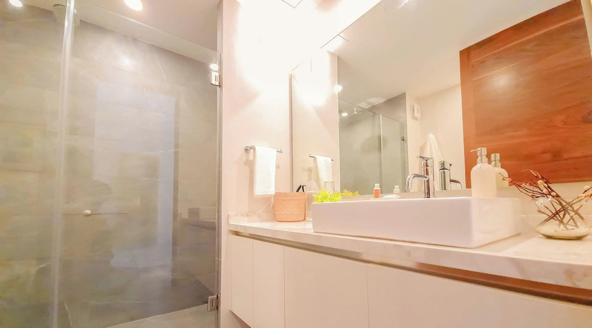 Un bagno moderno con box doccia in vetro, uno specchio grande e un lavandino bianco con articoli da toilette.