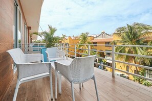 A balcony with a table and chairs, overlooking a residential area with palm trees and buildings. - 2BR w/ dual pools, near beach & 5th Ave (Playa del Carmen)