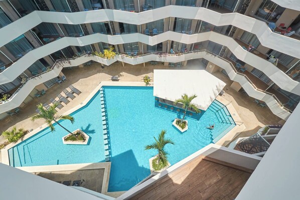 A multi-level hotel with a central swimming pool surrounded by lounge areas and outdoor seating. - 2BR w/ dual pools, near beach & 5th Ave (Playa del Carmen)