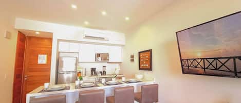 A modern kitchen with a dining area, equipped with a refrigerator, stove, and coffee maker.