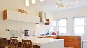 Eine moderne Küche mit weißen Schränken, einer zentralen Kochinsel, Holzstühlen und einem Deckenventilator.