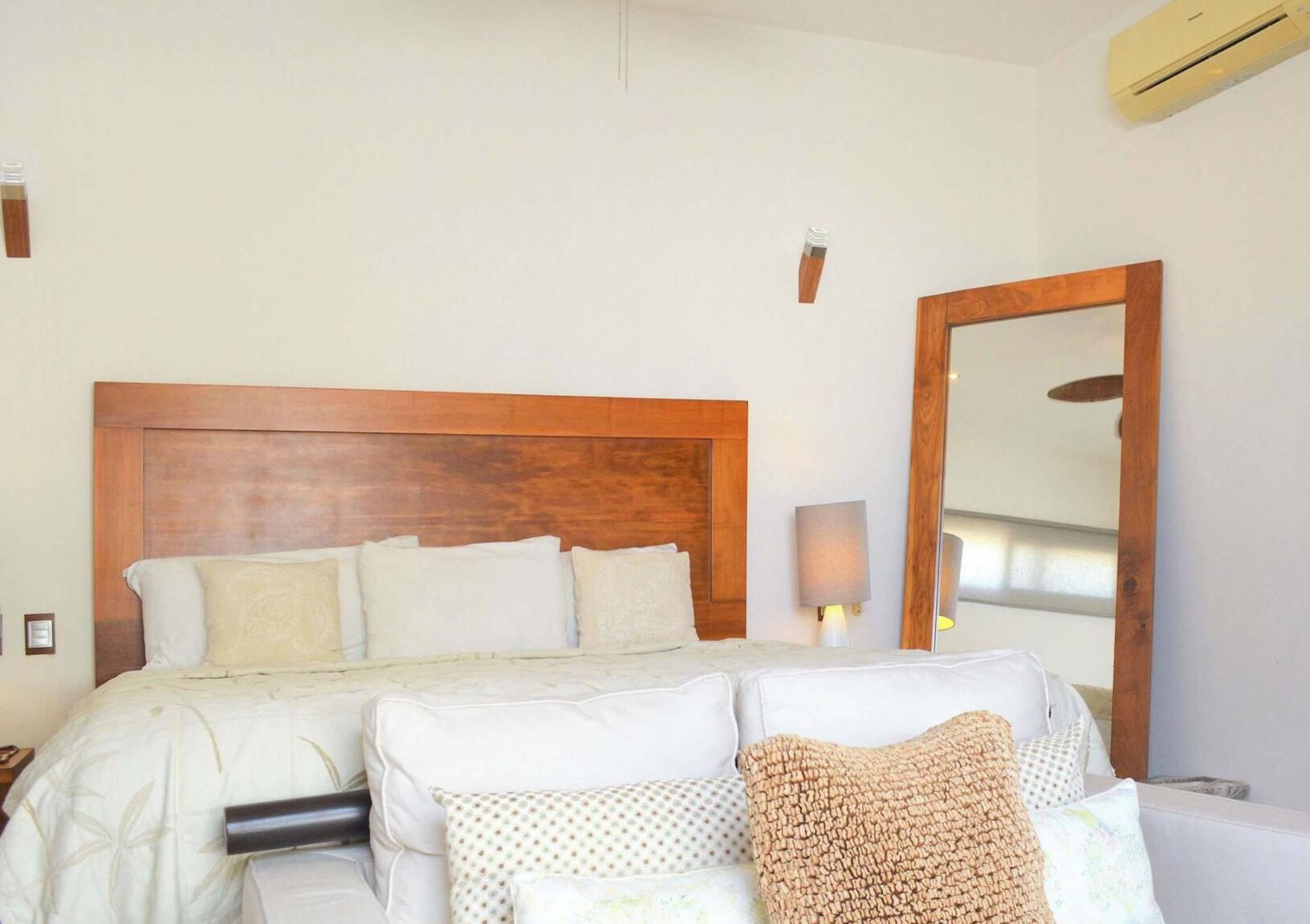 Une chambre d’hôtel avec une tête de lit en bois, un grand miroir et un lit doté de plusieurs oreillers.