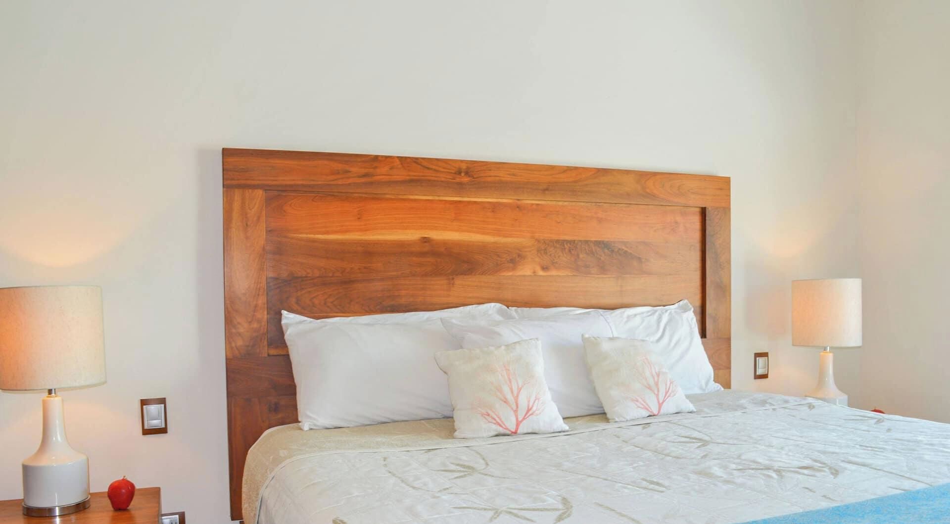 Una cama con cabecera de madera, dos lámparas de noche y una mesita de noche con una manzana roja.