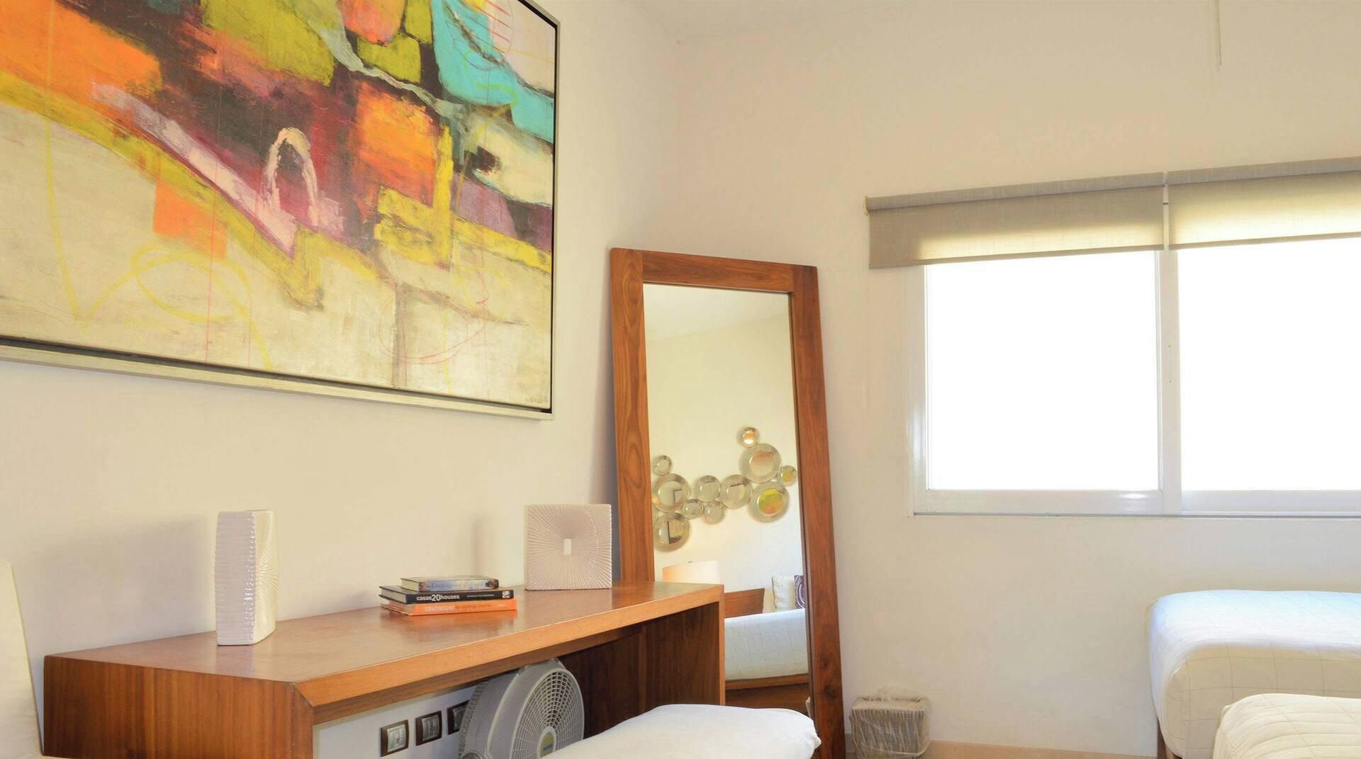 Habitación de hotel con cama, escritorio con espejo, una obra de arte en la pared y ventana con persianas.