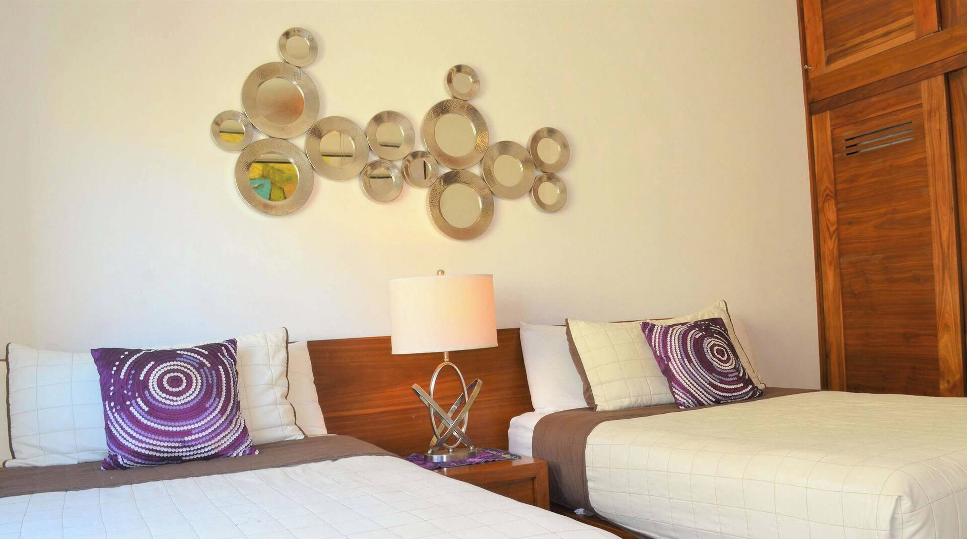 A hotel room with two beds, a nightstand, a lamp, and a wall decoration.