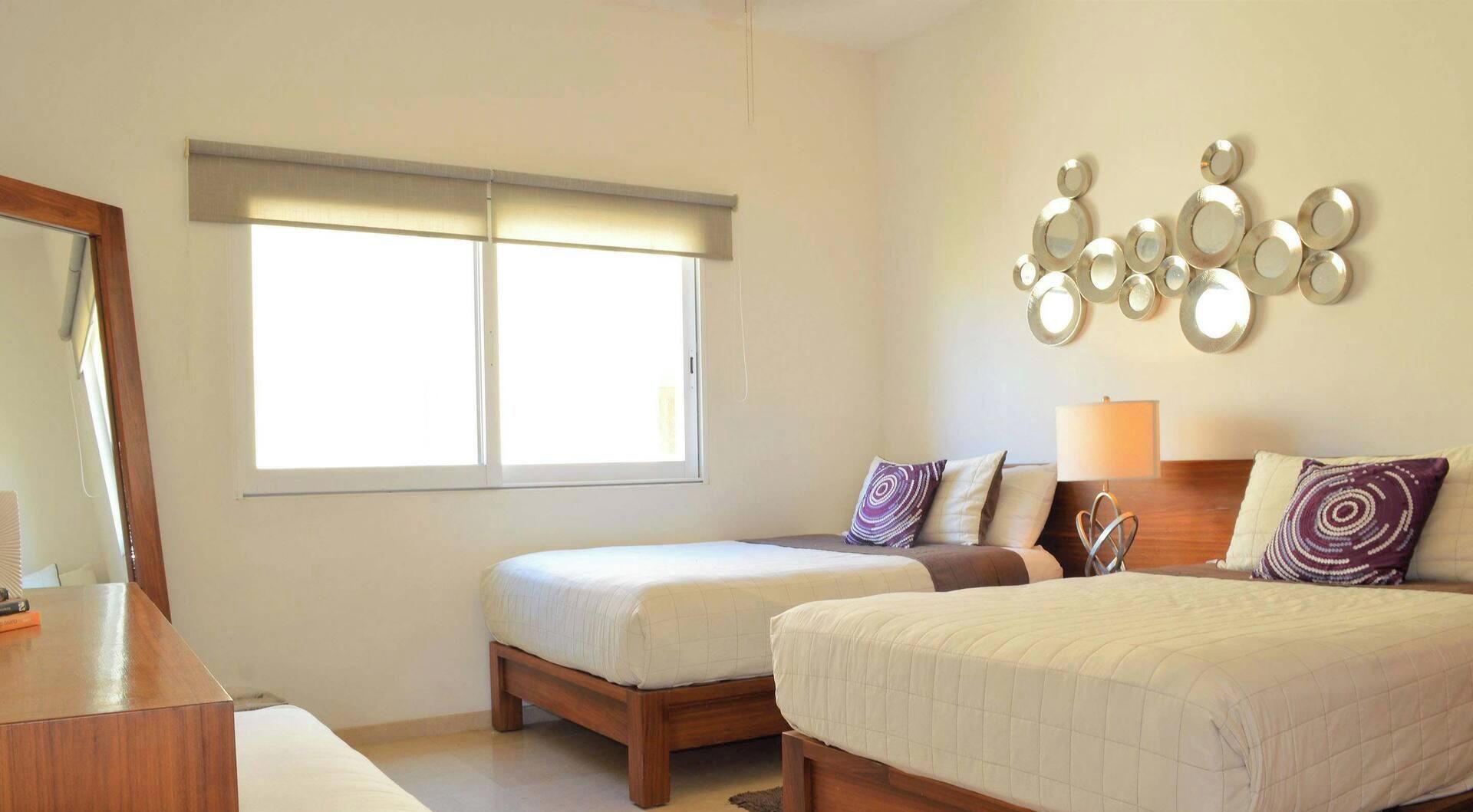 Habitación de hotel con dos camas, una mesita de noche, una lámpara y un espejo instalado en la pared.