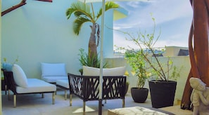 A balcony with a white sofa, a black woven chair, potted plants, and a Buddha statue. - Penthouse escape w/ hot tub & BBQ grill (Playa del Carmen)