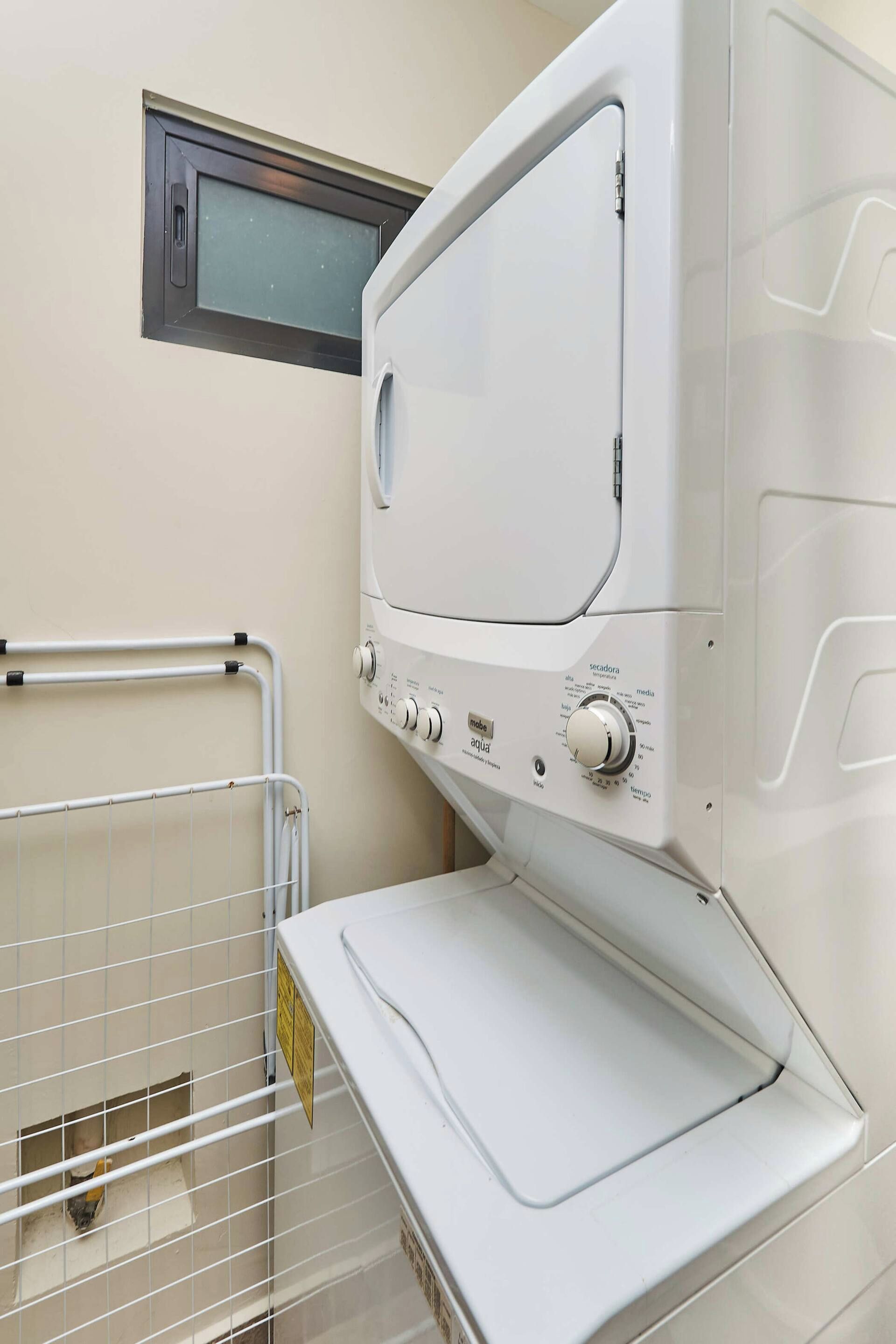 A white laundry machine with a control panel, a small window, and a metal rack.