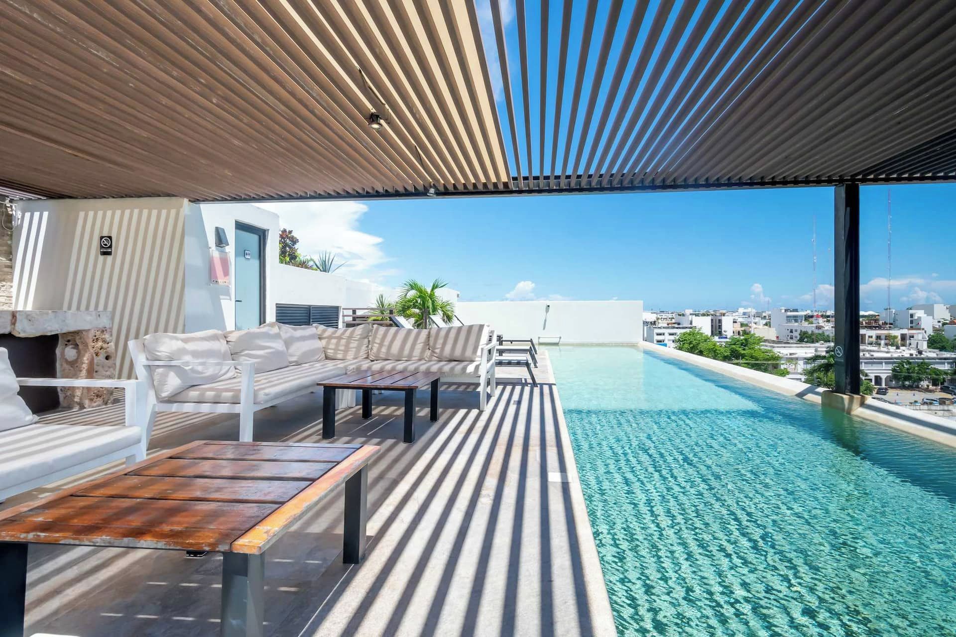 A rooftop infinity pool with a wooden deck, a sofa, and a table.