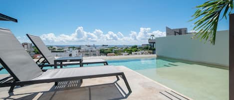 A rooftop pool area with lounge chairs and a view of the cityscape.