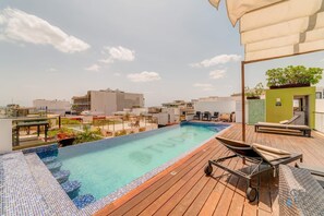 A rooftop pool with a wooden deck, lounge chairs, and a view of the cityscape. - Coastal oasis w/ spa tub near beach & 5th Ave (Playa del Carmen)
