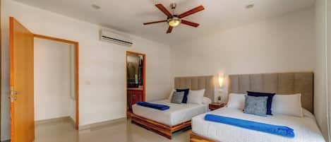A hotel room with two beds, a ceiling fan, an air conditioning unit, and a wooden door.