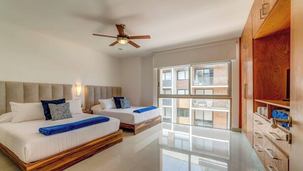 A hotel room with two beds, a ceiling fan, a large window, and a wooden wardrobe. - Coastal oasis w/ spa tub near beach & 5th Ave (Playa del Carmen)