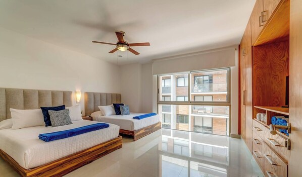 A hotel room with two beds, a ceiling fan, a large window, and a wooden wardrobe. - Coastal oasis w/ spa tub near beach & 5th Ave (Playa del Carmen)