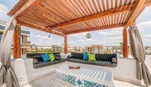 Ein Sitzbereich im Freien mit einer Holzpergola, zwei Sofas mit Kissen und einem Tisch mit einem Tablett Gläser.