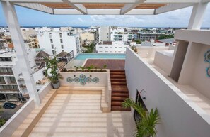 A rooftop terrace with a pool, surrounded by buildings, and a view of the sea. - Beachside escape w/ rooftop pool access (Playa del Carmen)