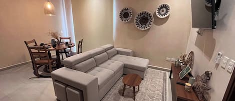 Een moderne woonkamer met een hoekbank, een eettafel met stoelen, decoratieve wandkunst en een plafondventilator.