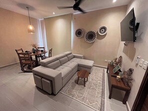 A modern living room with a sectional sofa, a dining table with chairs, decorative wall art, and a ceiling fan. - Beachside escape w/ rooftop pool access (Playa del Carmen)