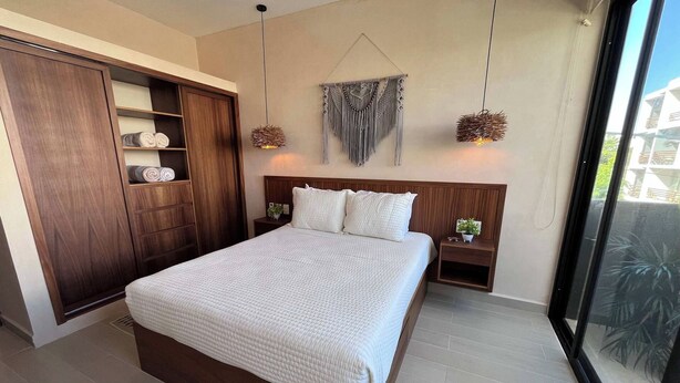 Una camera da letto moderna con un letto grande, un armadio in legno e un arazzo macramè appeso al muro.