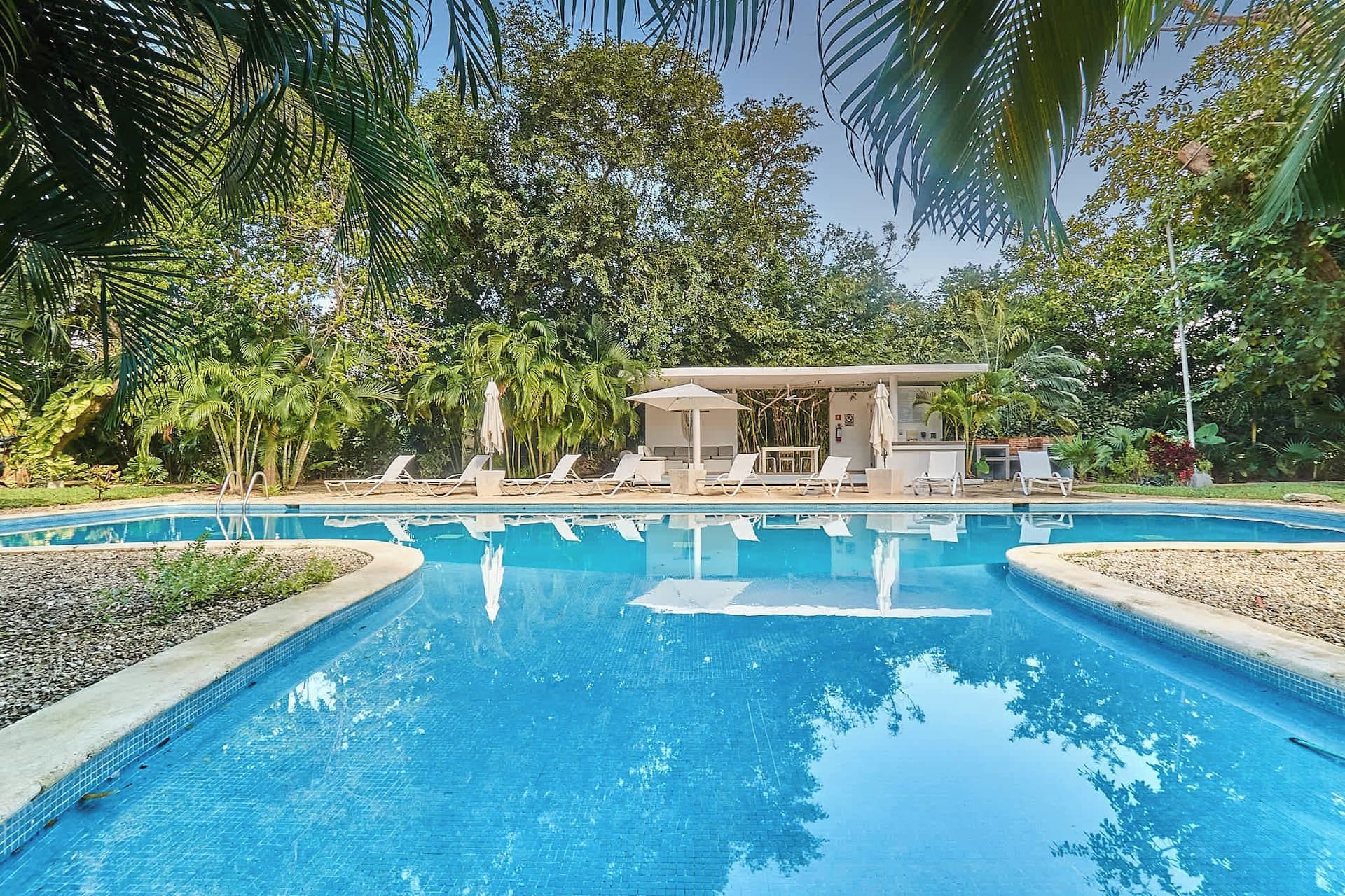 A swimming pool with lounge chairs and a covered seating area surrounded by lush greenery.
