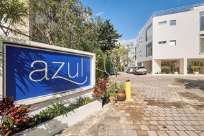 Ein blaues Schild mit dem Wort 'azul' an einem Gebäude, umgeben von Grünpflanzen und einer gepflasterten Straße.