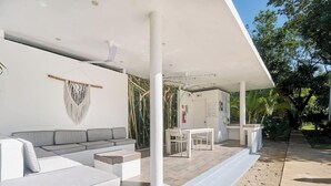 A covered outdoor seating area with a sofa and table, surrounded by greenery. - 3BR condo w/ pool & BBQ grill (Playa del Carmen)