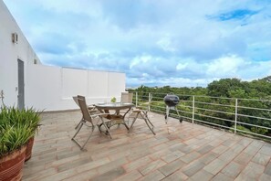 Una terrassa al terrat amb una taula rodona i cadires, una barbacoa i plantes en testos.