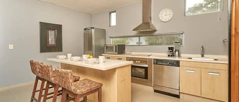 Une cuisine moderne dotée d’un îlot central, d’appareils électroménagers intégrés et d’une grande fenêtre.