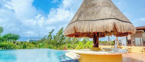A swimming pool with a thatched umbrella, wooden deck, and a view of the ocean.
