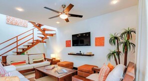 Ein modernes Wohnzimmer mit Treppe, Flachbildfernseher und Deckenventilator.