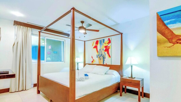 A four-poster bed with a ceiling fan, a window with curtains, a bedside table with a lamp, and a painting on the wall. - Penthouse w/ private terrace & rooftop pool (Playa del Carmen)