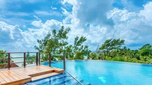 A clear blue sky with clouds, a wooden deck, and a swimming pool surrounded by lush greenery. - Penthouse w/ private terrace & rooftop pool (Playa del Carmen)