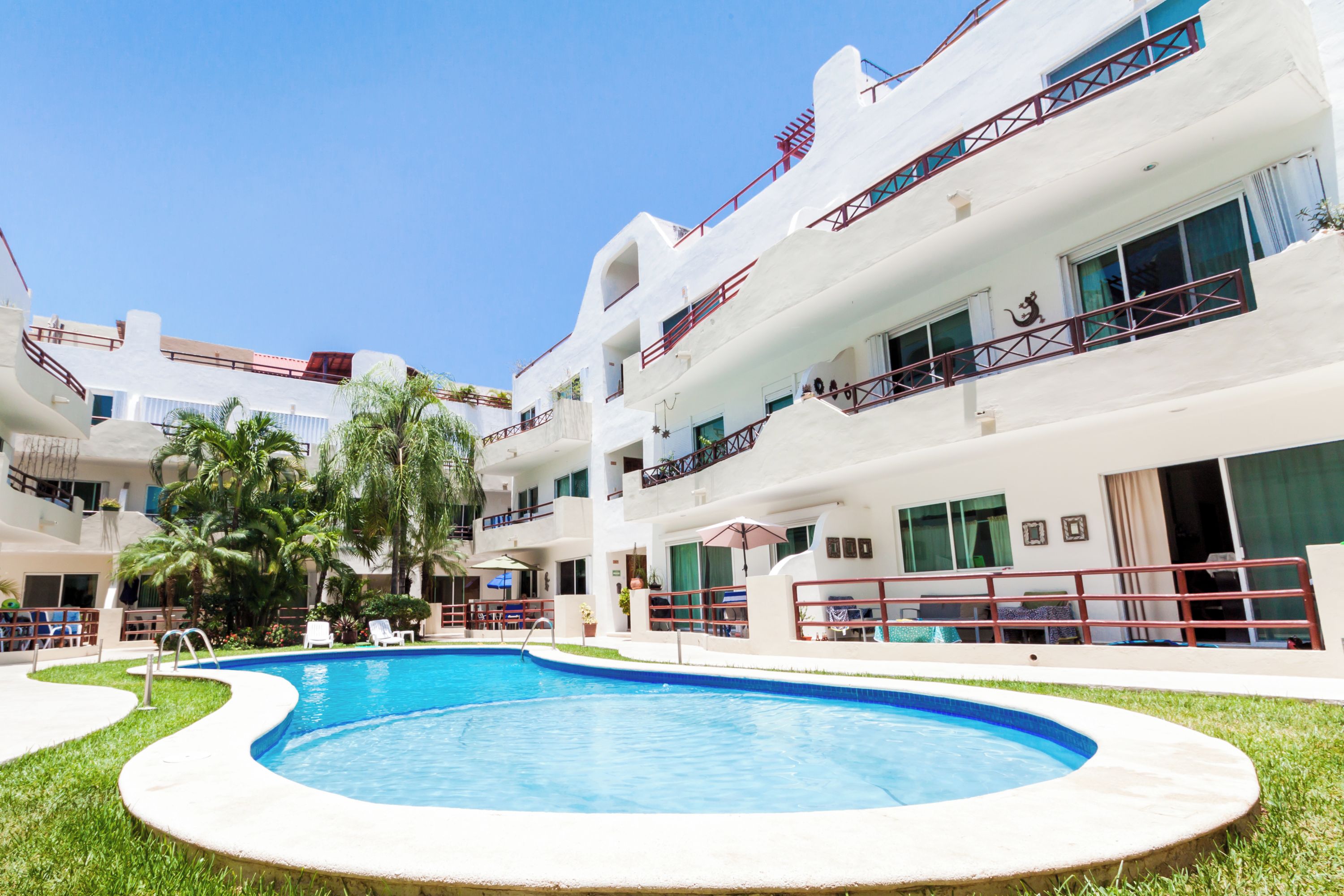 Un hotel con piscina, varios balcones y un cielo azul despejado.