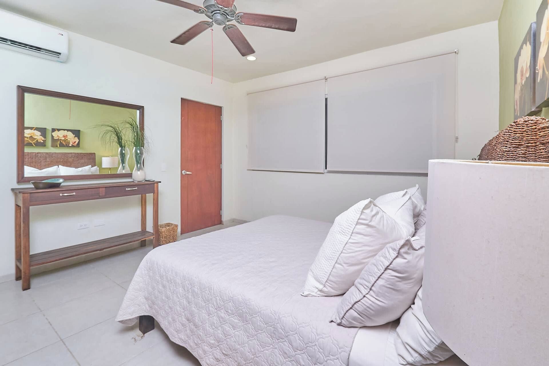 Un dormitorio con cama, cómoda, espejo, ventilador de techo y armario.