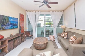 A living room with a sofa, a coffee table, a TV, and a ceiling fan. - 2BR condo - pool, BBQ & beach steps away (Playa del Carmen)